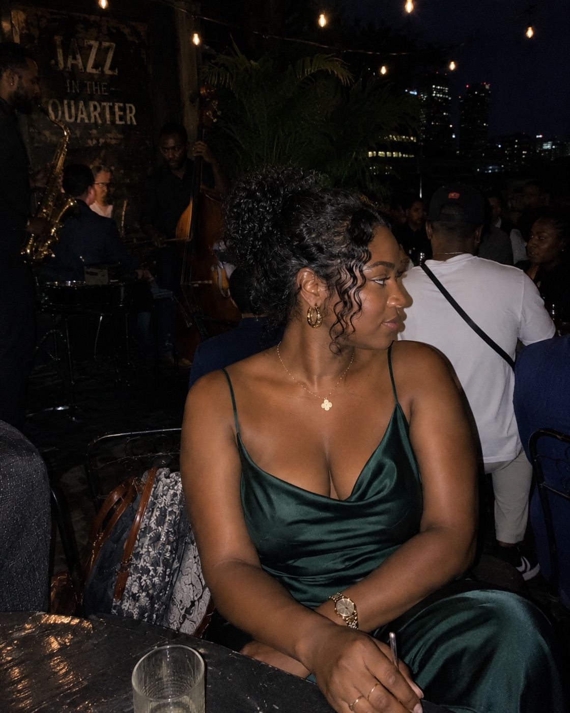 Woman in a dark green satin dress standing in an evening courtyard.