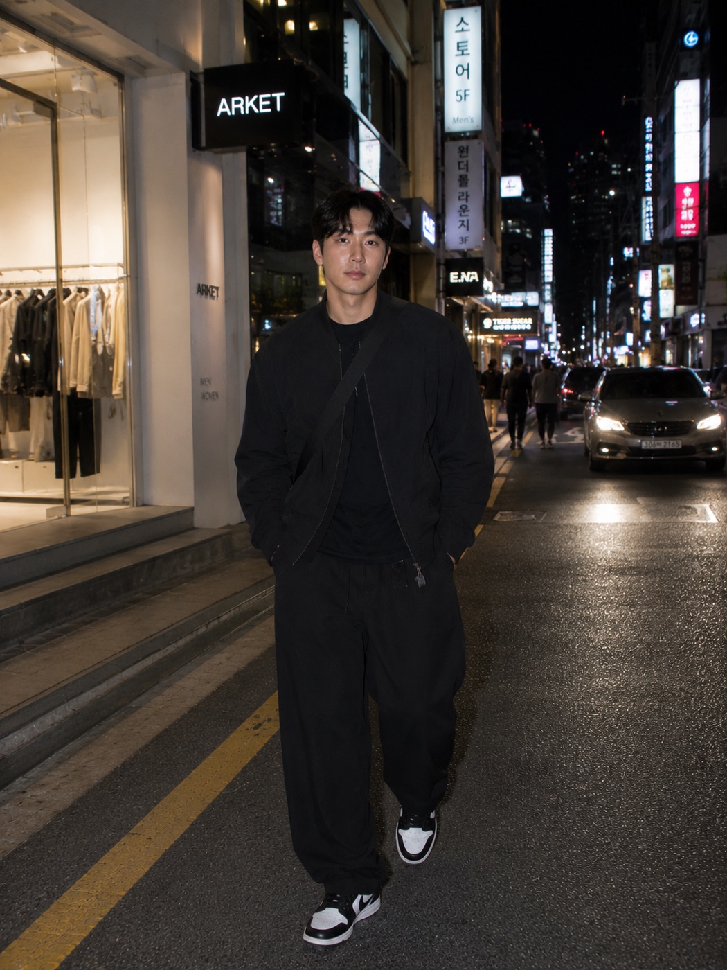 Man in black streetwear walking on a night street in Seoul.